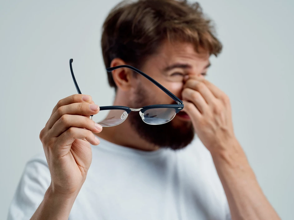 muž s unavenými očami držiaci dioptrické okuliare