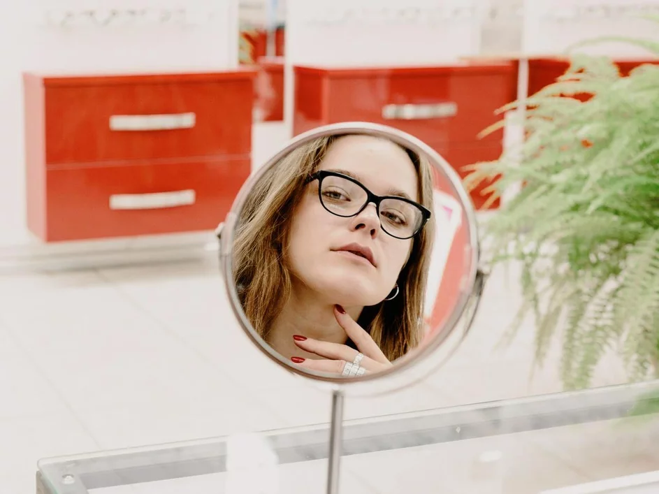 žena pozerajúca sa do zrkadla pri výbere okuliarov v optike žena pozerajúca sa do zrkadla pri výbere okuliarov v optike
